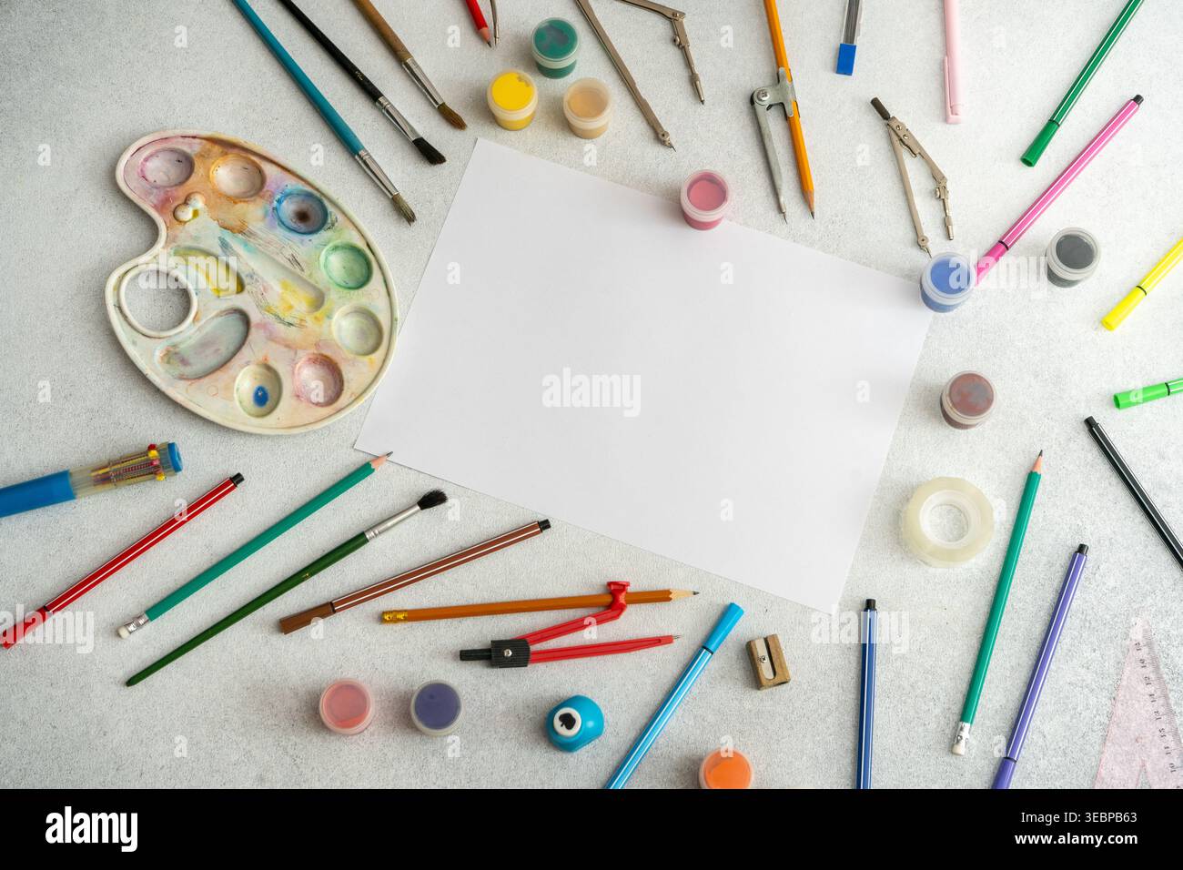 Scrivania Creative Art Workspace con un foglio bianco bianco bianco bianco bianco di pallet colorato di acquerello dipinge matite, pennelli e strumenti di disegno. Vista dall'alto dello sfondo dello studio scolastico Foto Stock