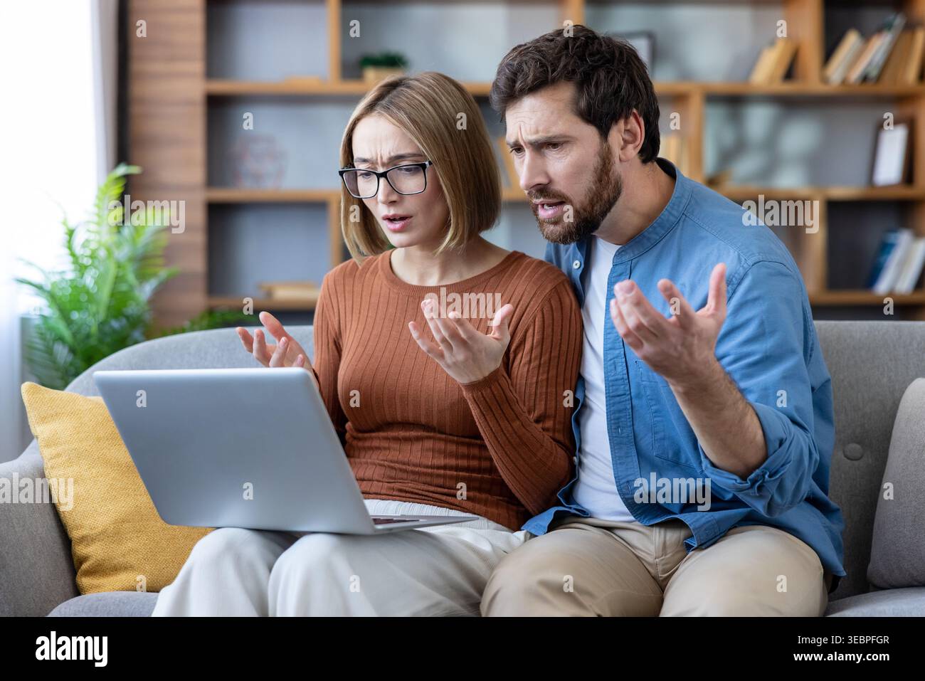 Coppia preoccupata che guarda un notebook con espressioni preoccupate, parla di cattive notizie o di una situazione difficile legata a problemi finanziari, debito o un Foto Stock