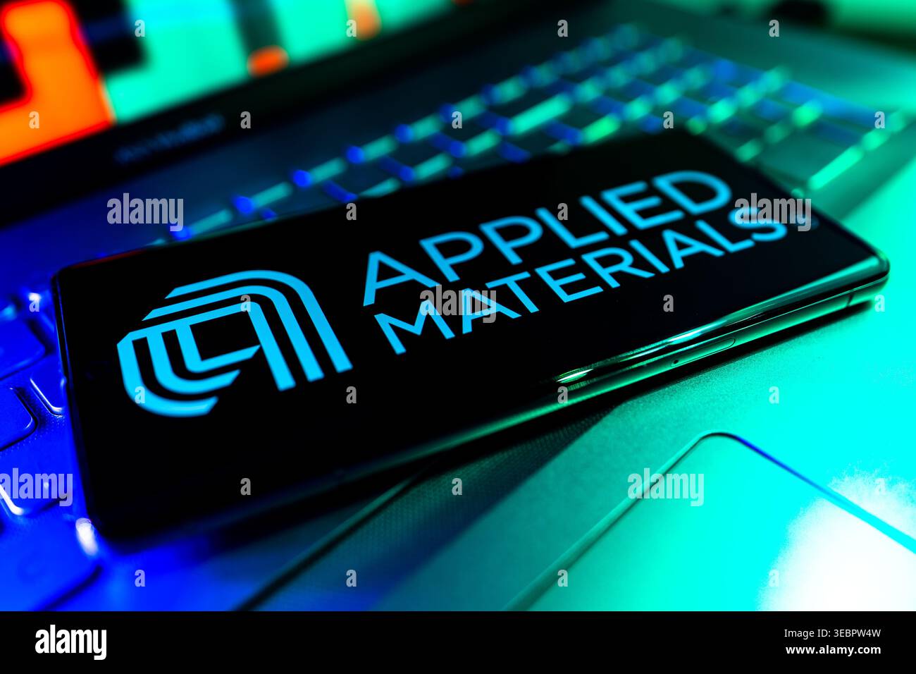 Logo della società di apparecchiature per semiconduttori dei materiali applicati visualizzato sullo schermo con sfondo del grafico delle prestazioni finanziarie del mercato azionario Foto Stock