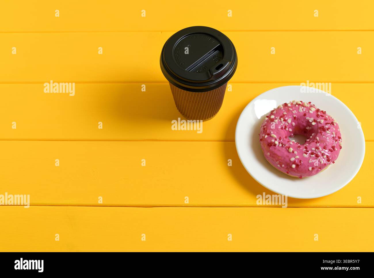 Ciambella rosa con goccioline e tazza da caffè nera su sfondo giallo in legno Foto Stock