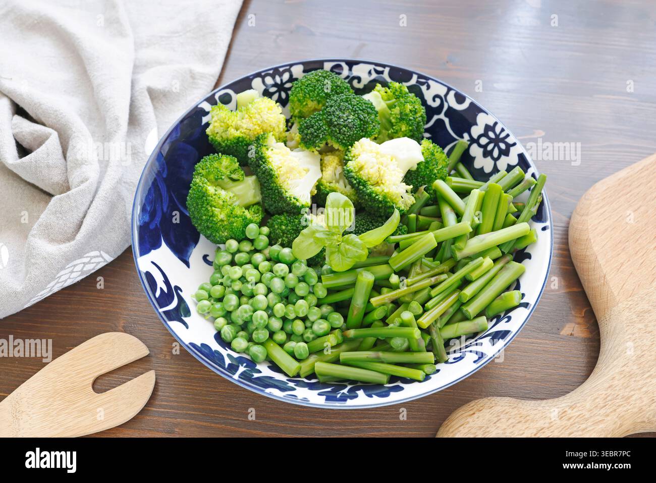 Verdure verdi fresche nella ciotola in ceramica mediterranea. La tendenza alimentare sana e sostenibile presenta broccoli al vapore, piselli e lance di asparagi per Foto Stock