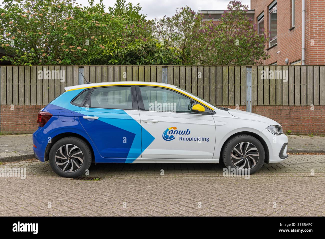Utrecht, Paesi Bassi, 13 aprile 2026. Profilo laterale di un'auto scolastica ANWB brandizzata, una Polo Volkswagen bianca, parcheggiata lungo una recinzione di legno nel c Foto Stock