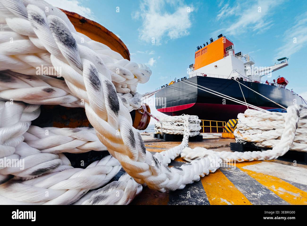 Funi di ormeggio grandi in primo piano con grande nave petroliera ancorata al porto. Foto Stock