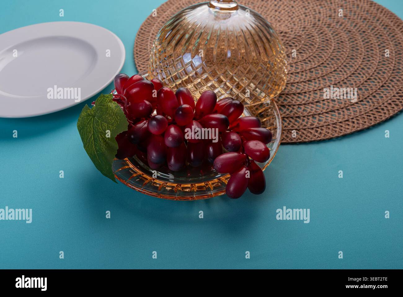 Studio STILL Life con uva da tavola senza semi cremisi servita su un piatto di vetro sotto un cloche di cristallo con tovaglietta testurizzata. Riprese con illuminazione soffusa Foto Stock