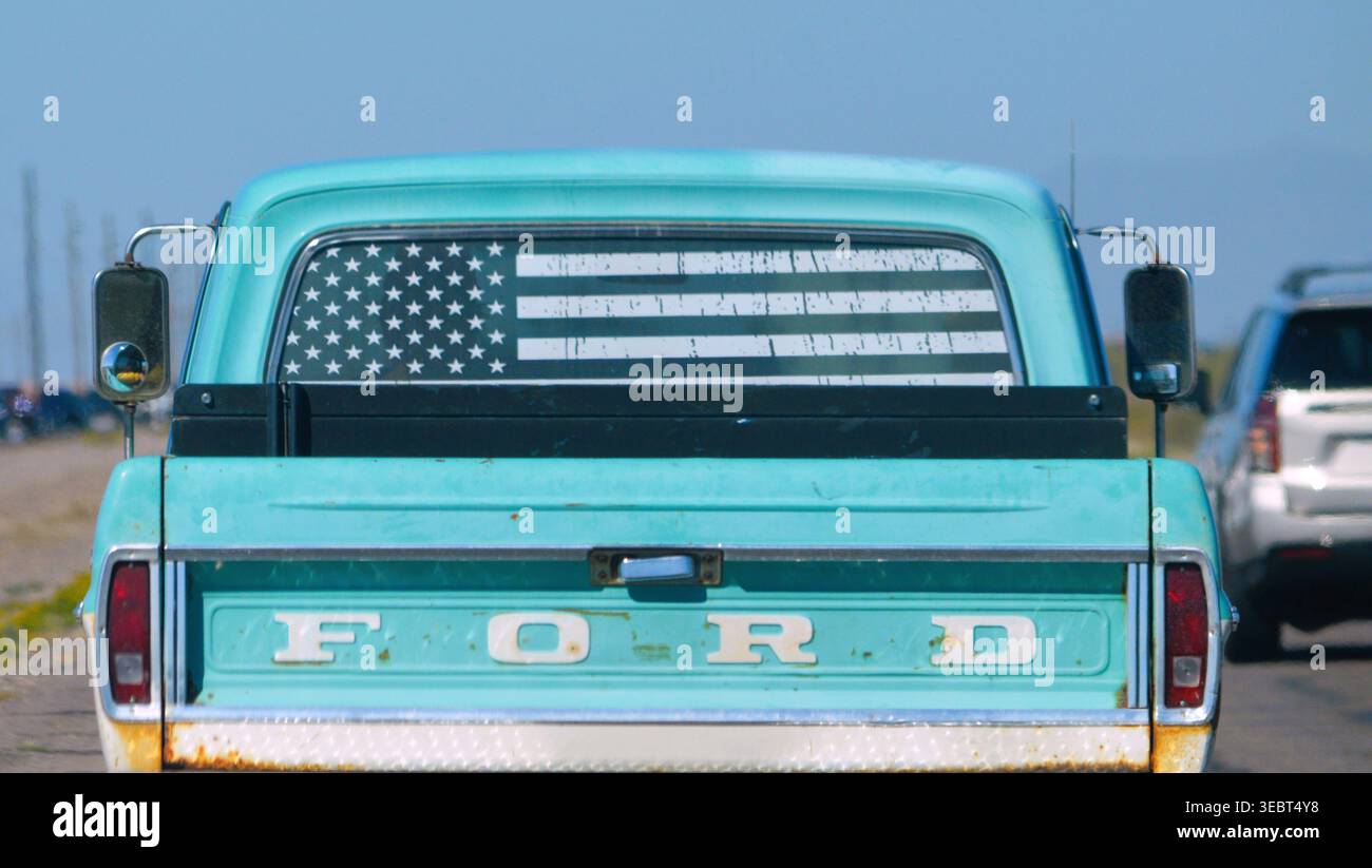 Phoenix, Arizona - 20 aprile 2026: Un classico pick-up Ford di colore turchese con bandiera americana sul lunotto, viaggia su un'autostrada rurale. Foto Stock
