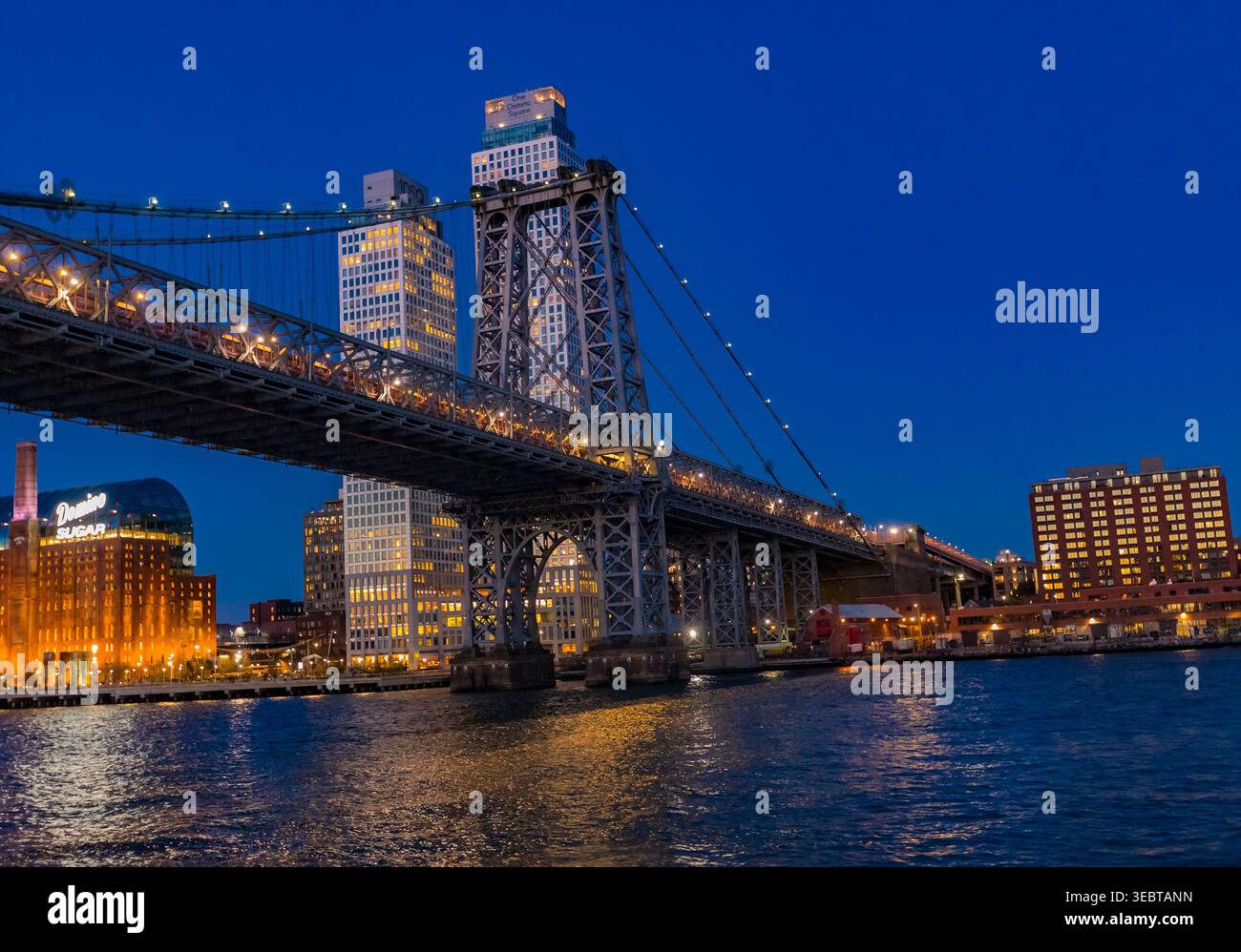 New York, Stati Uniti - 12 aprile 2026: Le torri d'acciaio illuminate del Williamsburg Bridge attraversano l'East River al crepuscolo. Quando il Williamsbu Foto Stock