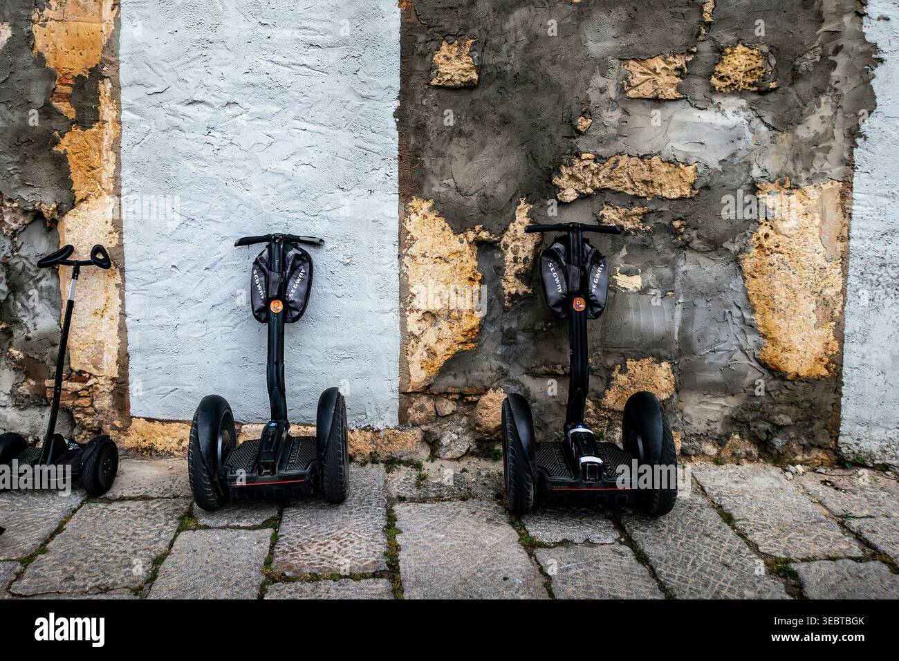 I mezzi di trasporto personali Segway parcheggiavano contro un muro di pietra sbriciolato e intempestivo a Cagliari. Il terreno è fatto di grandi ciottoli grigi. Foto Stock