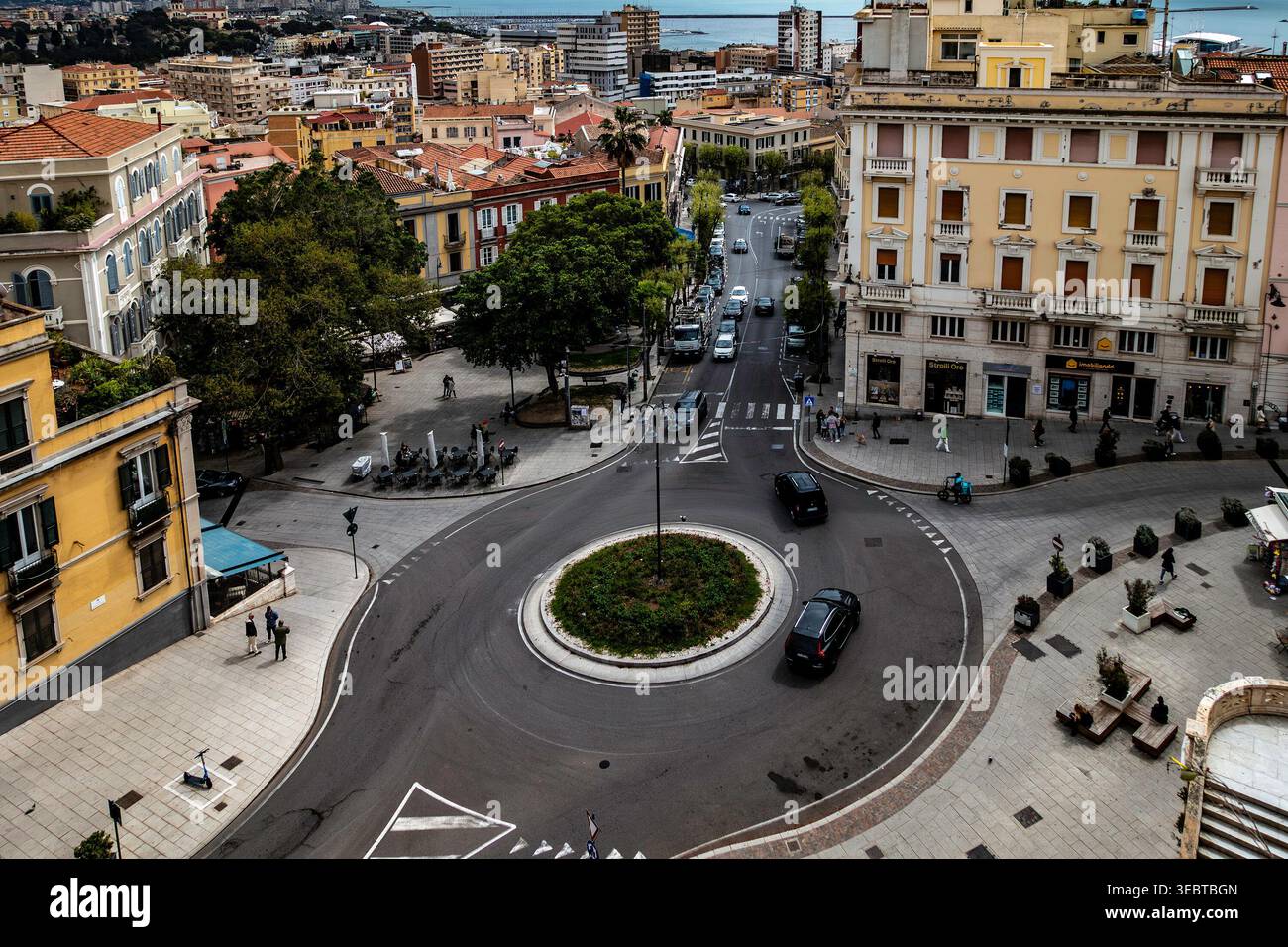 Una vista aerea di Piazza Yenne a Cagliari che mostra una rotonda centrale, edifici della città e strade con traffico. Alberi e pedoni sono visibili. Foto Stock