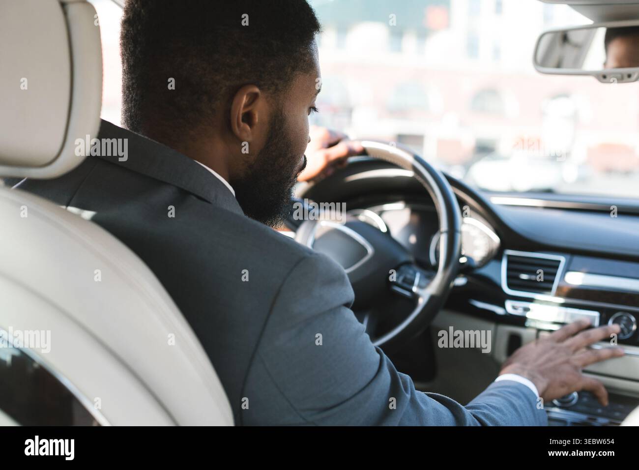 Autista professionista che naviga per le strade della città durante una giornata di sole a bordo di un veicolo di lusso Foto Stock