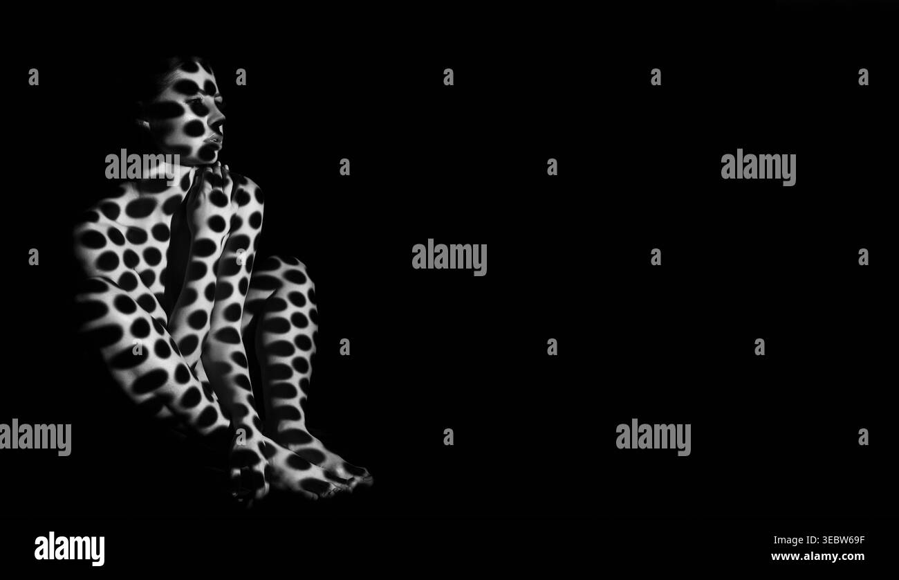 Espressione creativa attraverso la Body Art con design maculato in bianco e nero in condizioni di scarsa illuminazione Foto Stock