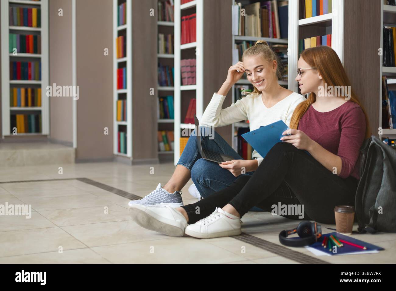 Amici che studiano insieme in una biblioteca seduti sul pavimento durante le ore diurne Foto Stock