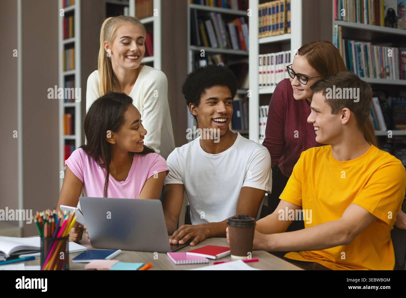 Gruppo di studenti che collaborano intorno a un notebook in un ambiente di libreria Foto Stock