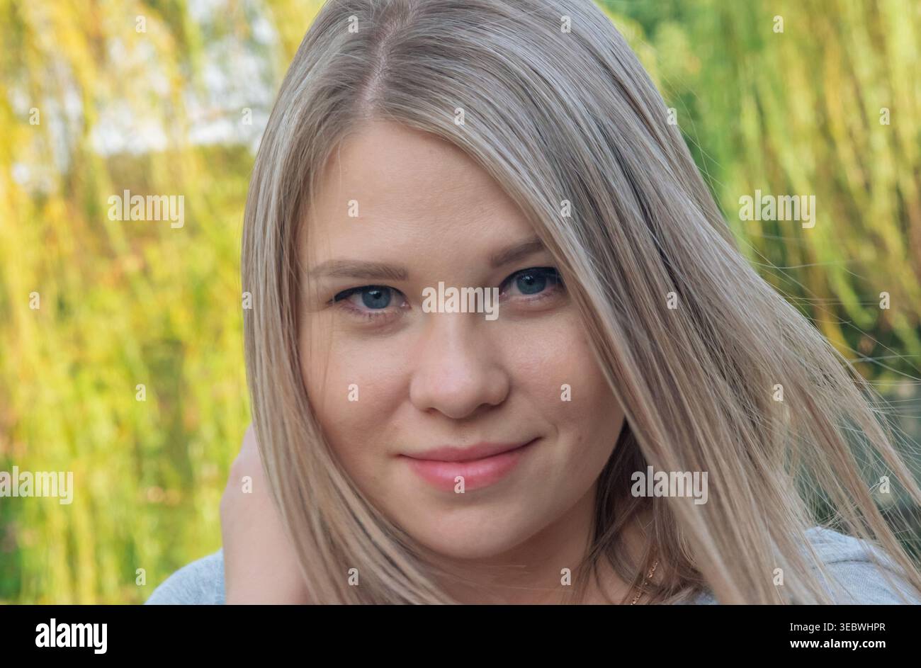 Colpo alla testa di una giovane donna con capelli biondi chiari e occhi blu all'aperto con luce naturale Foto Stock