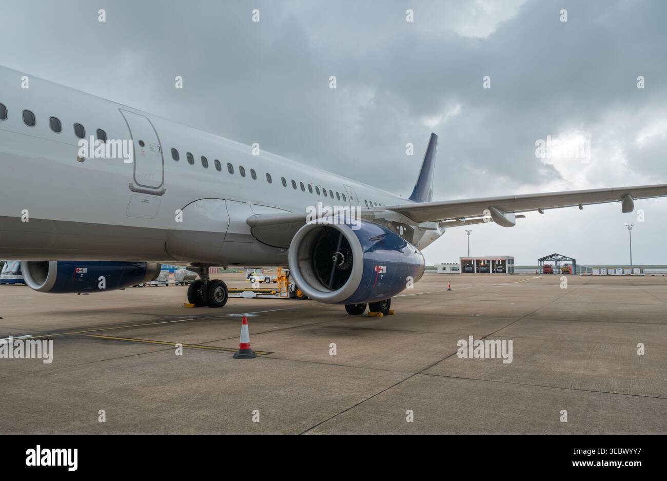 Jet di linea commerciale bianco parcheggiato sul grembiule dell'aeroporto con motore blu contro nuvole grigie Foto Stock