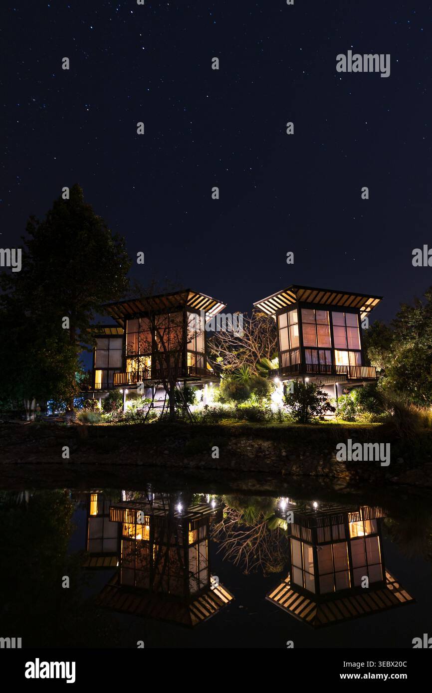 Due case moderne si illuminano sotto il cielo stellato notturno, riflessi sulla superficie del lago. Foto Stock