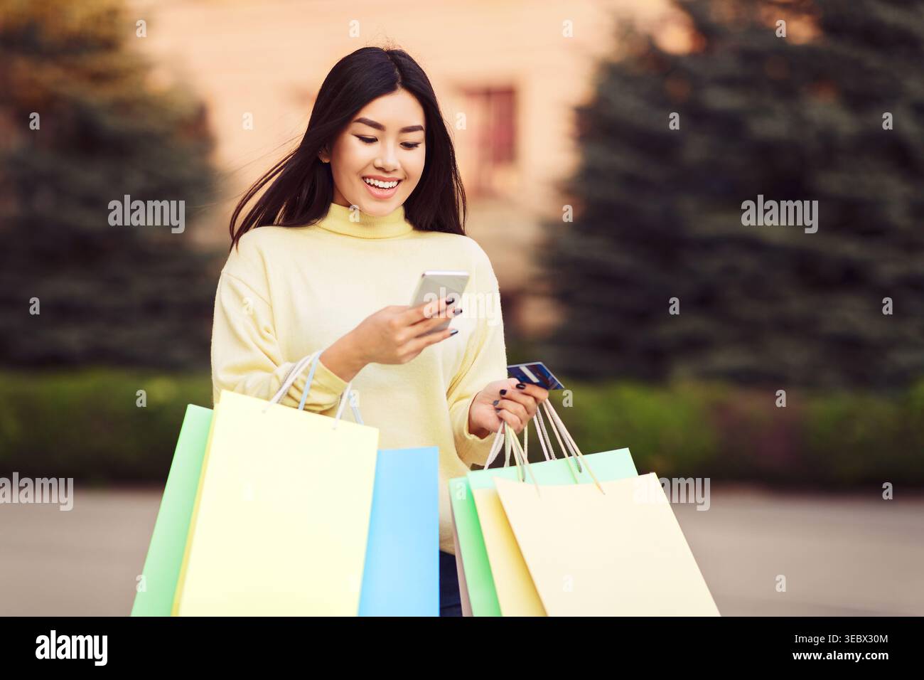 Una giovane donna ama fare shopping con le borse colorate mentre usa il suo smartphone all'aperto Foto Stock