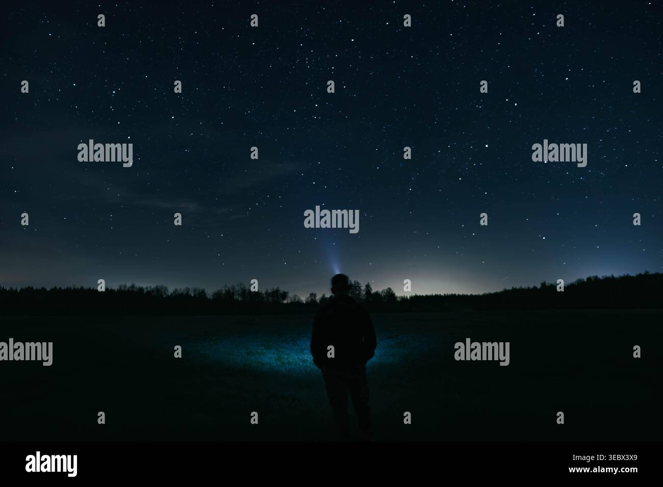 Un uomo con un faro che guarda il cielo stellato. Foto Stock