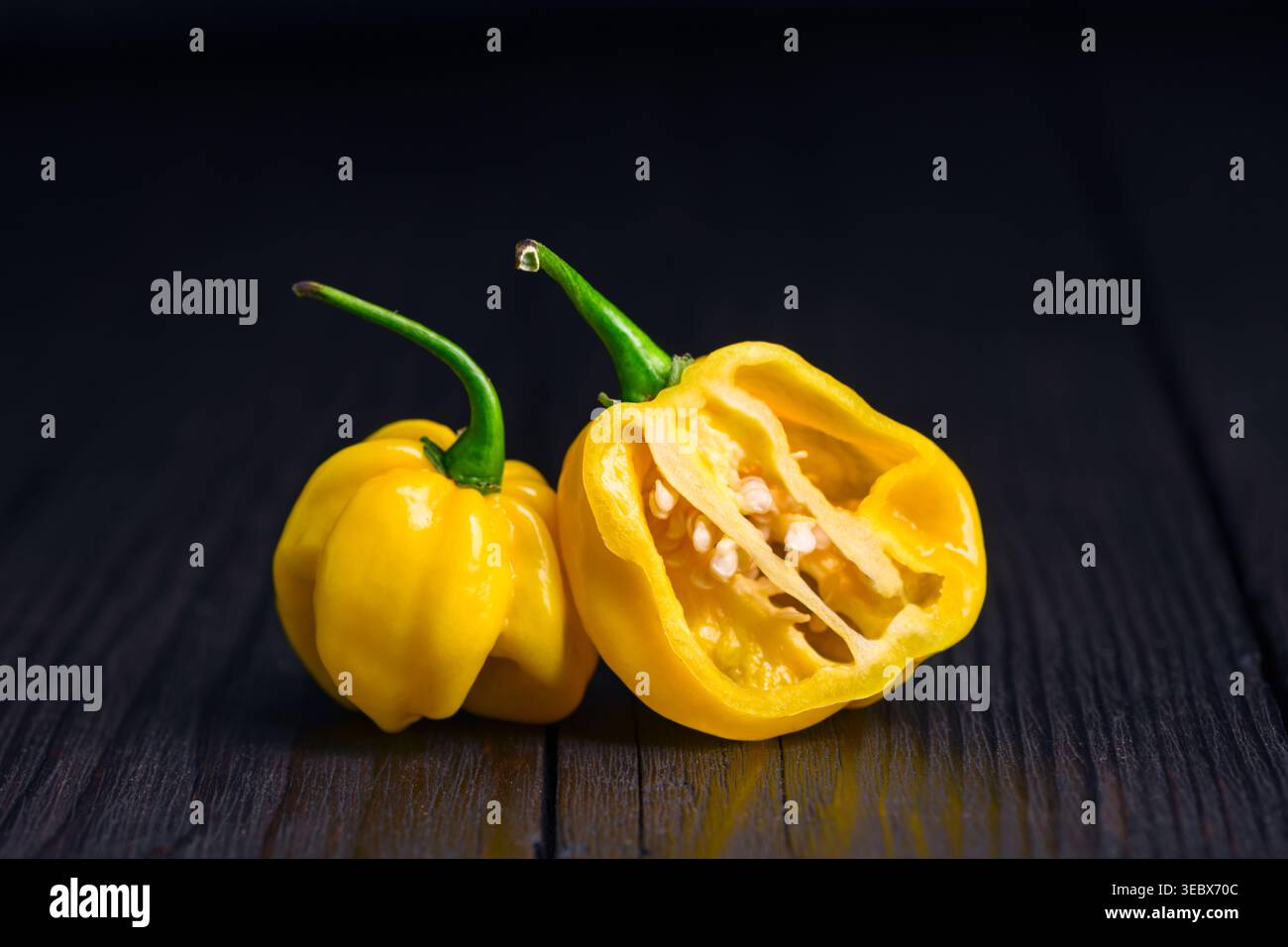 Peperoni habanero gialli con metà a fette su una superficie di legno. Gli interni delle cialde di peperoncino fresco presentano una composizione rustica Foto Stock