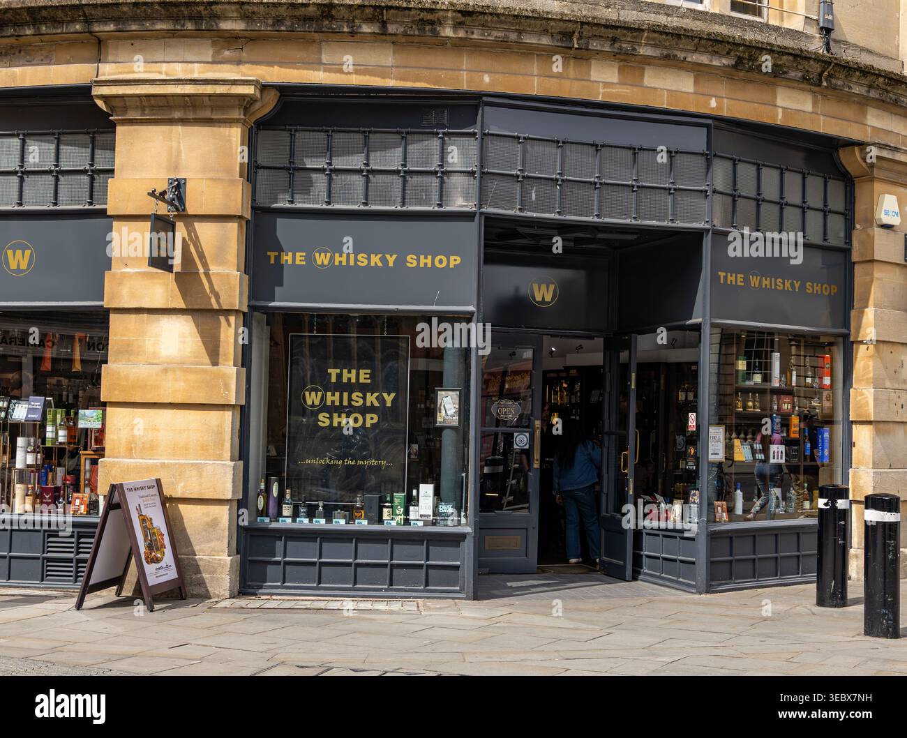 Vista esterna del negozio di whisky con architettura in pietra e mostra di alcolici in bottiglia nelle finestre di High Street Bath Foto Stock