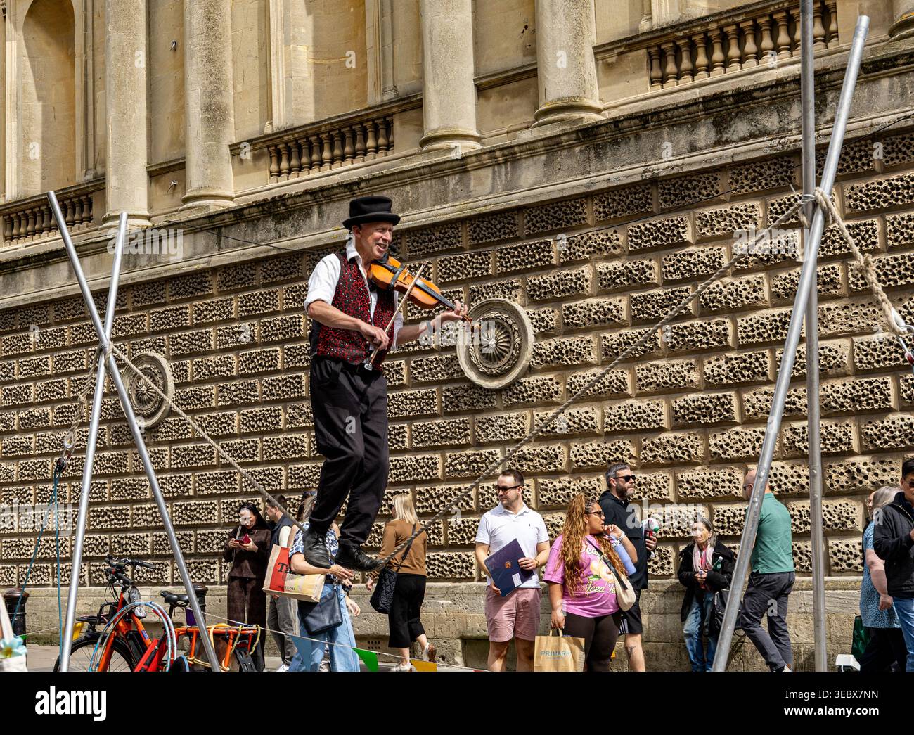 Artista di strada in equilibrio su una corda mentre suona il violino di fronte a uno storico edificio in pietra di Bath, Regno Unito Foto Stock