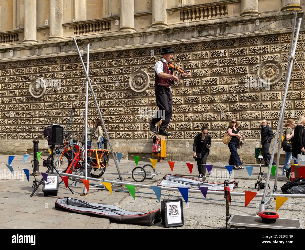 Artista di strada in equilibrio su una corda mentre suona il violino di fronte a uno storico edificio in pietra di Bath, Regno Unito Foto Stock