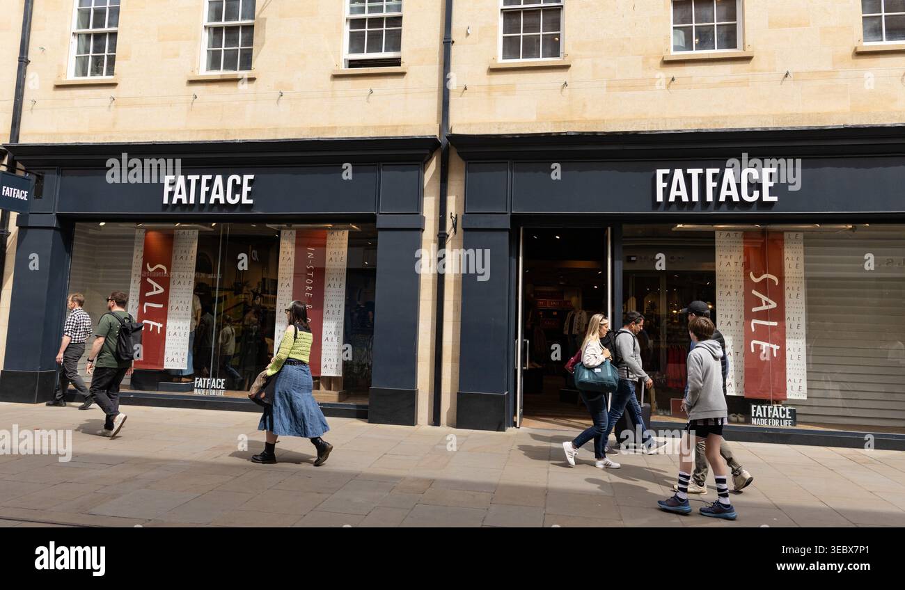 Gli amanti dello shopping passano davanti a un negozio di abbigliamento FatFace con cartelloni stagionali in vendita alle vetrine in una giornata di sole Green Street Bath UK Foto Stock