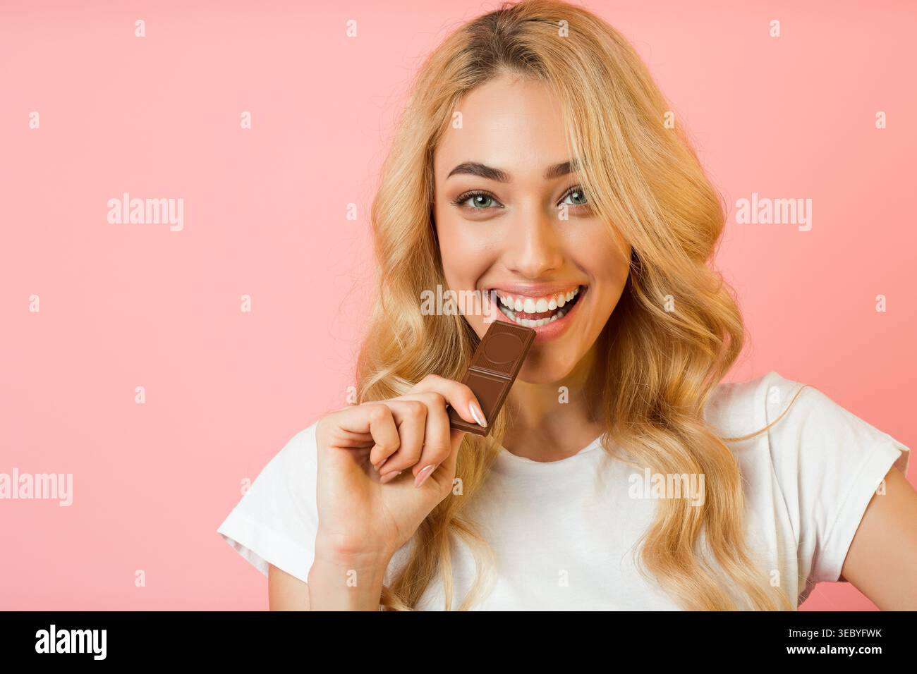 Donna sorridente che si gusta il cioccolato su uno sfondo rosa in un ambiente allegro Foto Stock