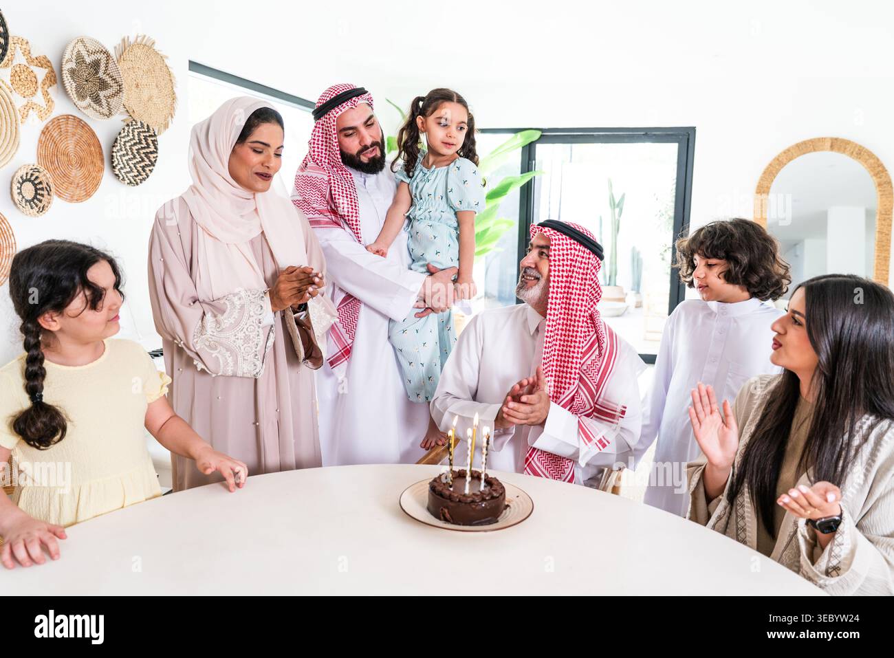 La famiglia araba si radunò intorno a un tavolo a casa, celebrando un compleanno con una torta al cioccolato, applaudendo e godendosi il momento felice della famiglia Foto Stock