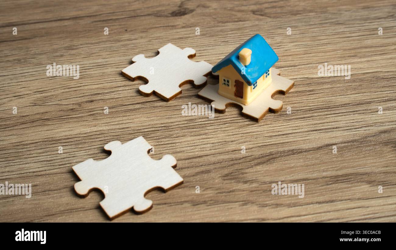 Modello di casa in miniatura posizionato su un puzzle in legno che rappresenta soluzioni immobiliari, ricerca di case e strategia di mercato immobiliare. Foto Stock