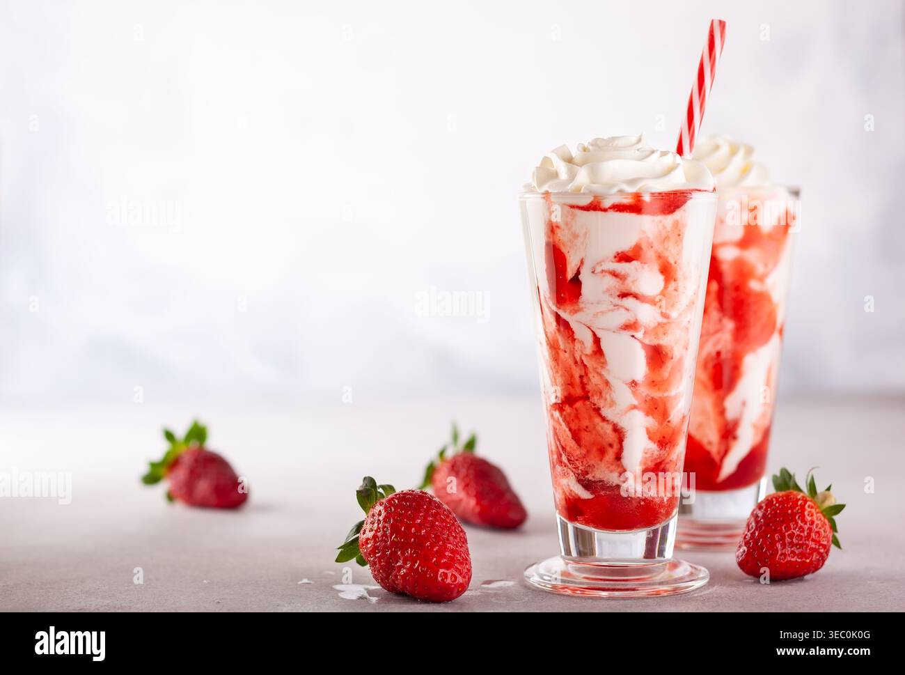 Frullato di fragole con panna montata e sciroppo di bacche nel bicchiere alto su sfondo chiaro. Foto Stock