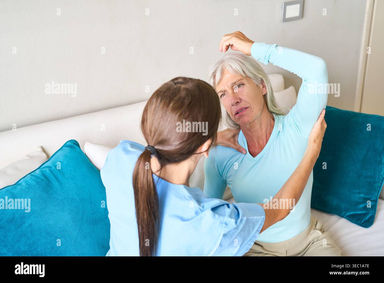 Assistenza sanitaria di alto livello e terapia fisica. Un'infermiera in scrub blu assiste una donna anziana con dolore alla spalla, guidandola attraverso la riabilitazione da sforzo Foto Stock