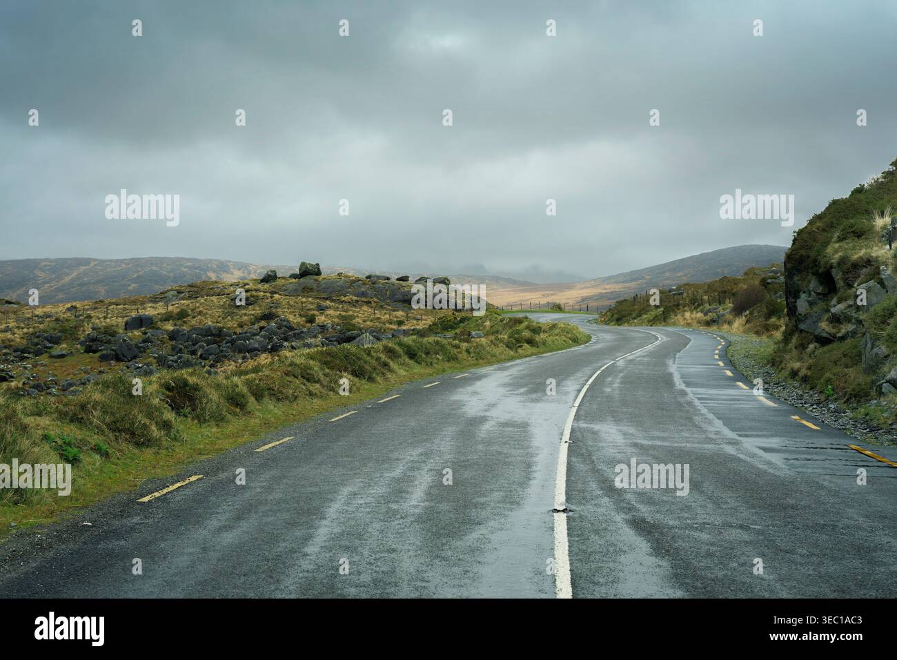 Strada di montagna curvilinea N71 che attraversa il suggestivo paesaggio glaciale della contea di Kerry, in Irlanda, in una giornata nebbiosa. Foto Stock