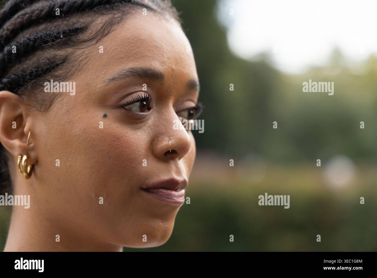 Donna afroamericana che guarda a destra con trecce di corvo, cerchio dorato, doppio cerchio nel parco Foto Stock