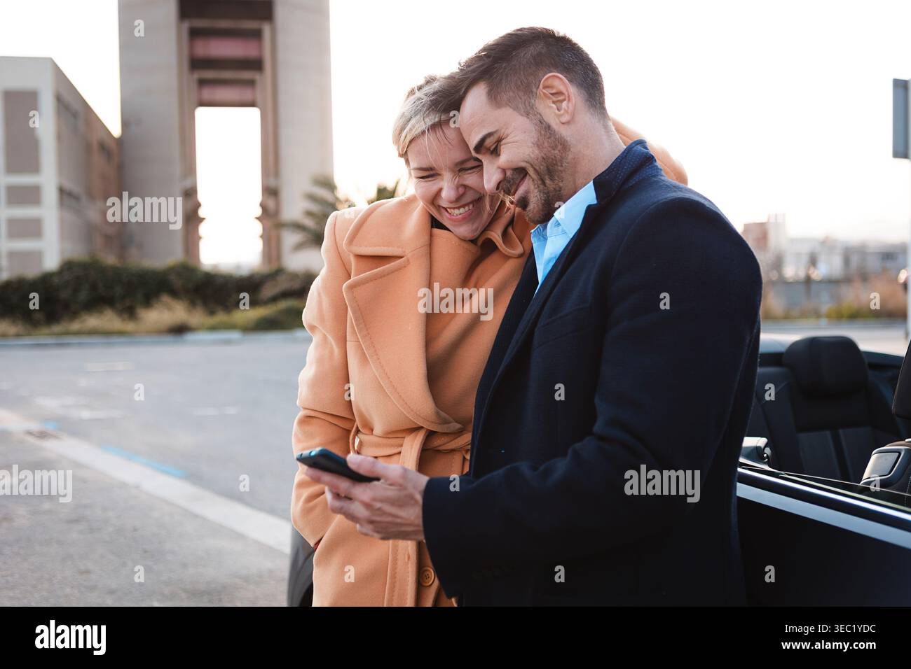 Felice coppia di adulti che guarda uno smartphone vicino a un'auto convertibile Foto Stock