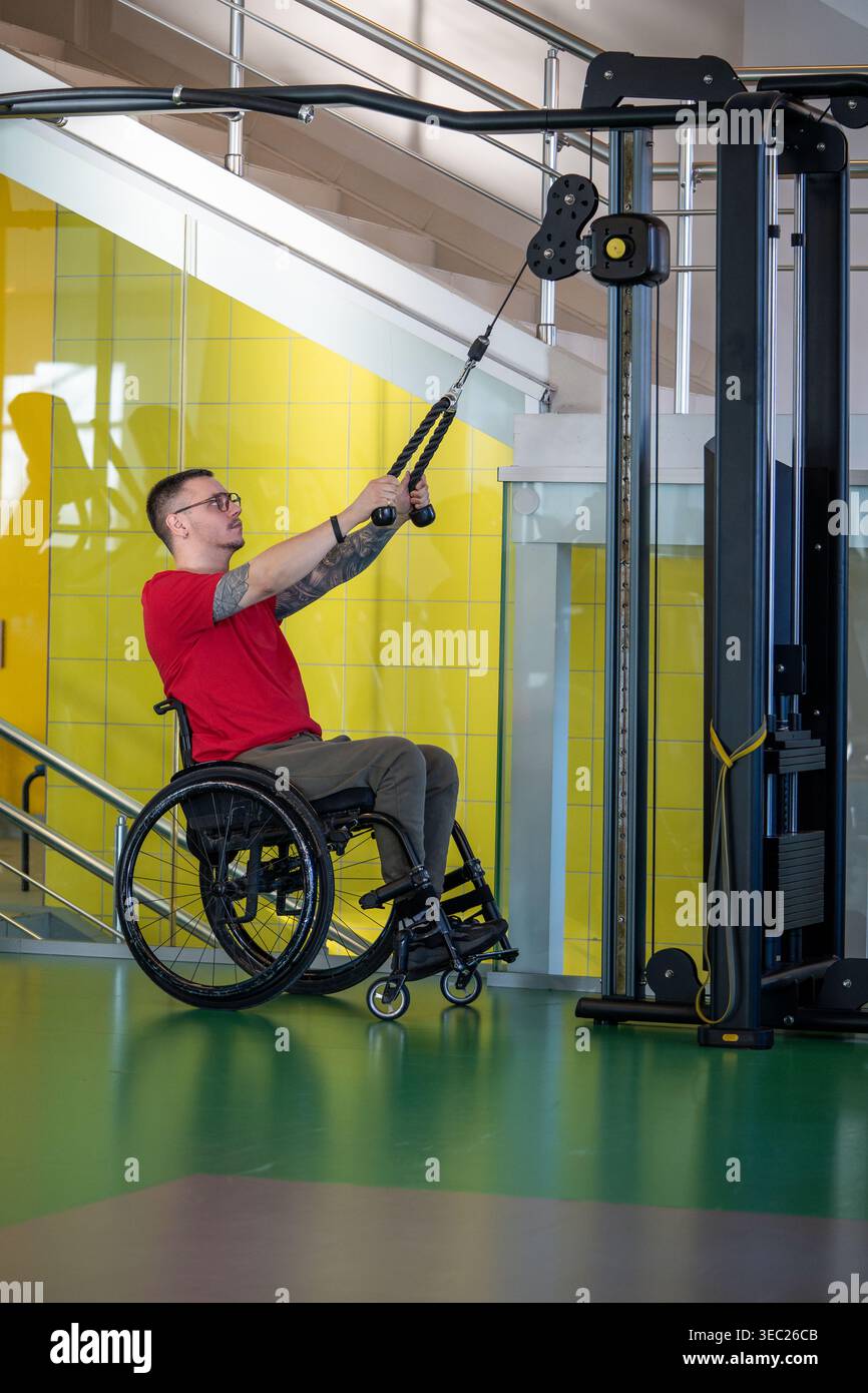 Uomo disabile motivato che allena i muscoli superiori del corpo con una macchina sportiva per la terapia Foto Stock