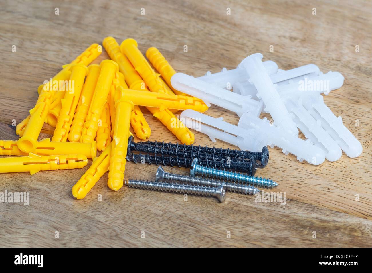 Ancoraggi a parete in plastica e viti metalliche posizionate su una superficie in legno, che mostrano i comuni dispositivi di fissaggio utilizzati per il montaggio a parete, le riparazioni domestiche, la costruzione Foto Stock