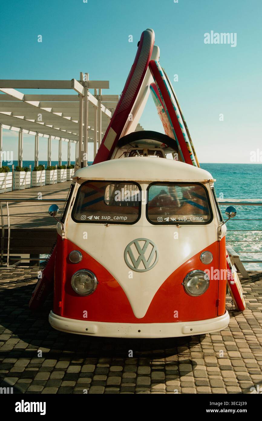 Volkswagen vecchio stile parcheggiata lungo la tranquilla passeggiata sul lungomare con tavole da surf e piastrelle luminose Foto Stock