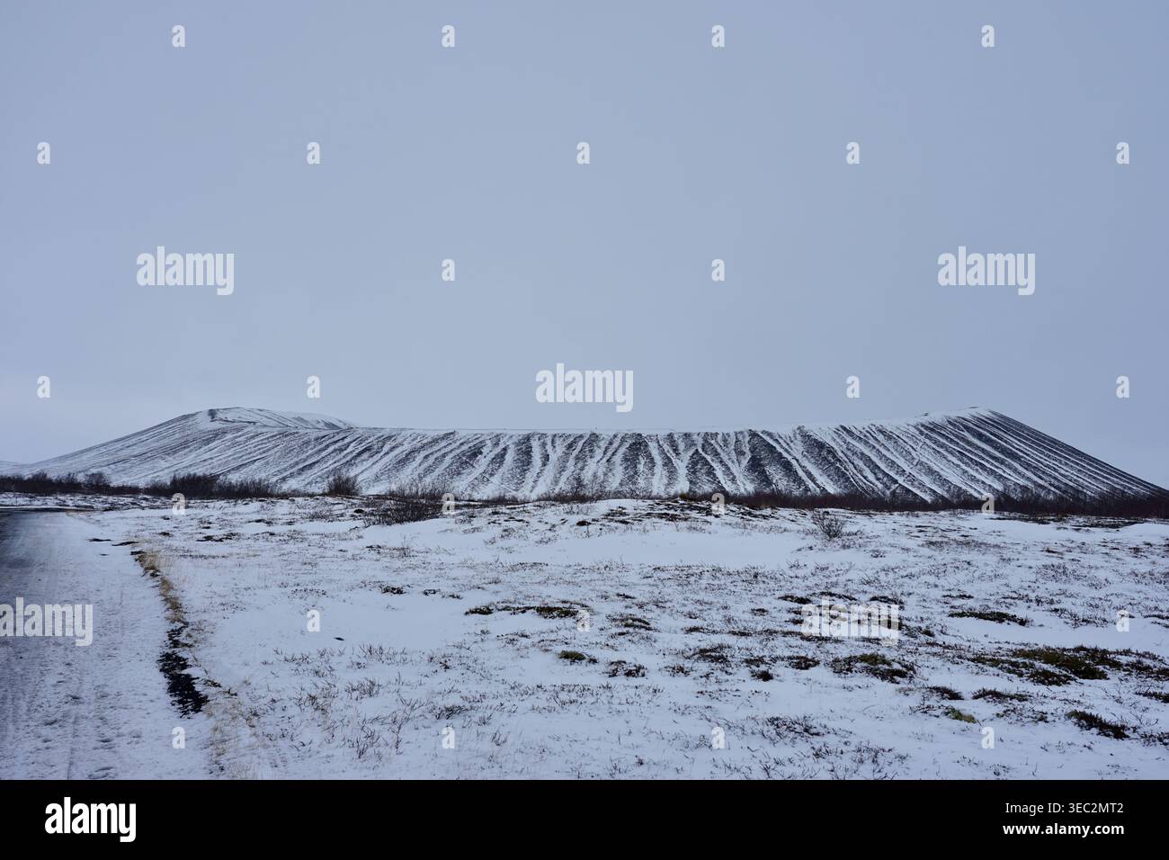 Paesaggio innevato della collina vulcanica sotto il cielo coperto con piste striate e primo piano vuoto Foto Stock