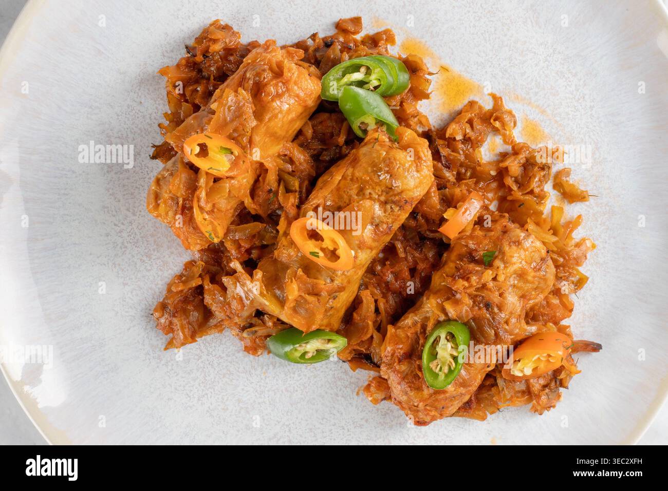 Piatto di tradizionali rotoli di cavolo su cavolo tritato, decorato con peperoncino a fette su un piatto rotondo su un chiaro sfondo di marmo. Foto Stock