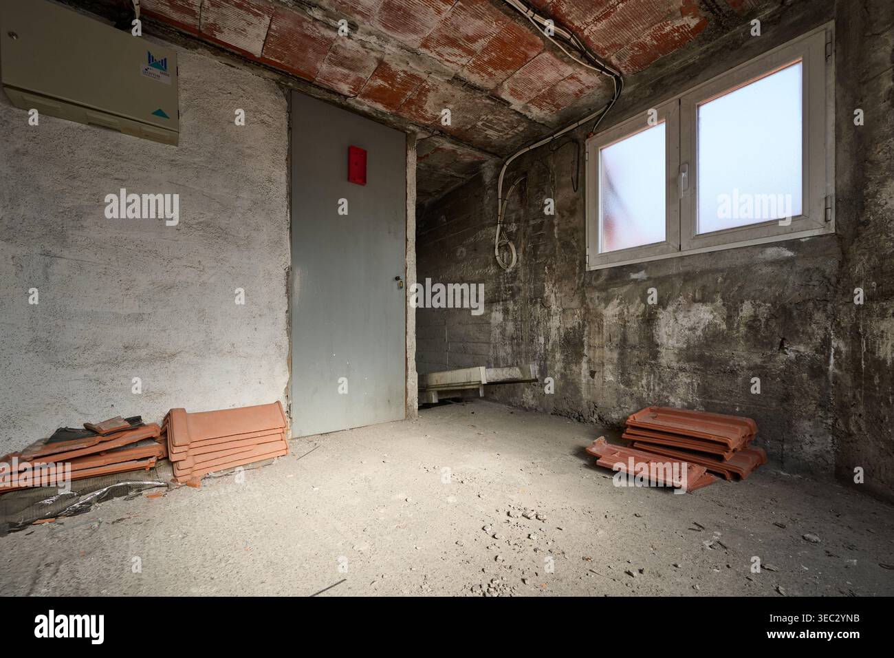 Pareti in cemento grezzo e soffitto in mattoni a vista in una stanza vuota e incompiuta durante la costruzione o la ristrutturazione con tegole Foto Stock