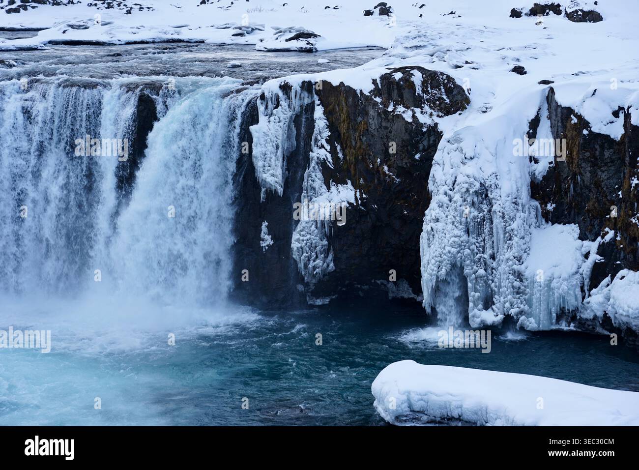 Cascata ghiacciata e scogliere ghiacciate nel paesaggio invernale innevato con il fiume Turchese Foto Stock