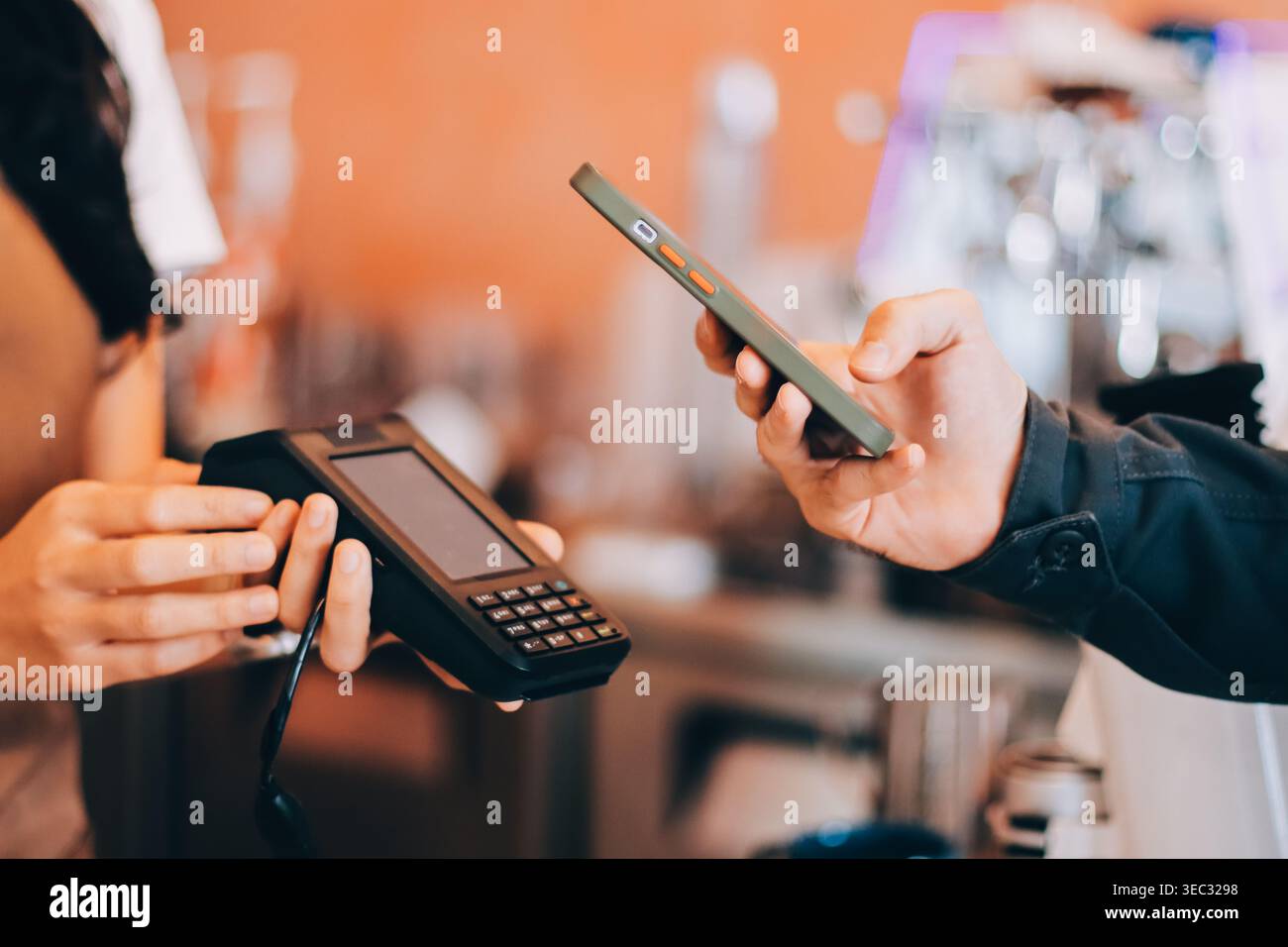 Barista asiatica anziana che riceve pagamenti mobili da un cliente tramite smartphone presso un bar che dimostra una moderna transazione senza contanti in un ambiente accogliente Foto Stock