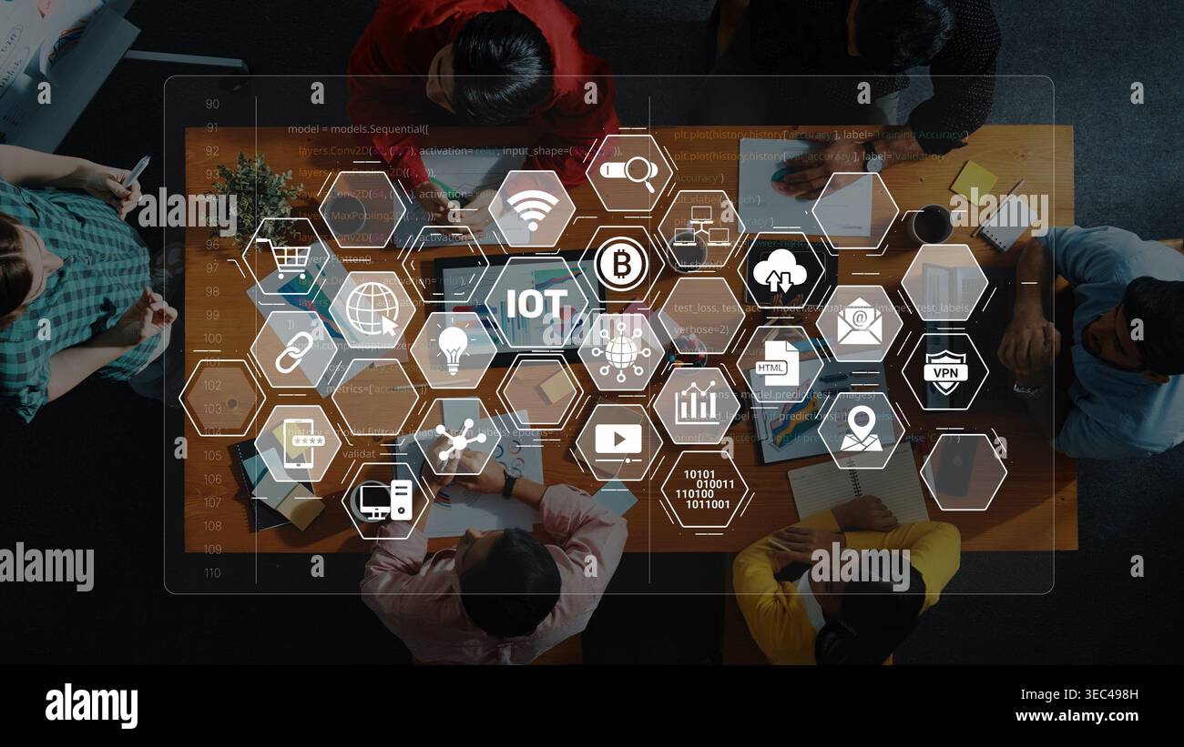 Un team eterogeneo partecipa a una riunione strategica, analizzando la tecnologia IoT con icone digitali visualizzate su un moderno tavolo di lavoro Foto Stock
