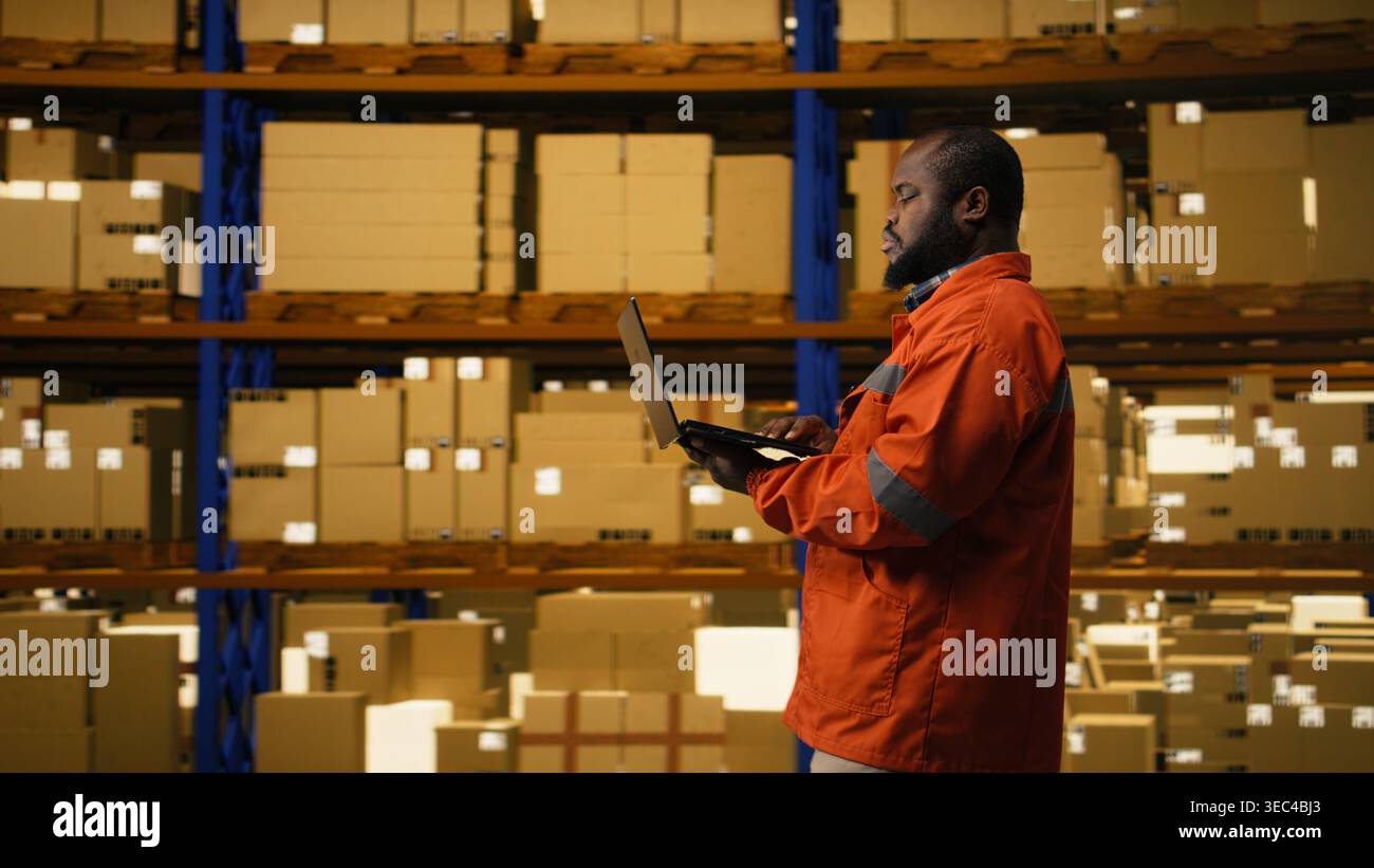 Evasione degli ordini su computer portatile, personale afroamericano, gestione delle spedizioni da parte dei dipendenti in impianti industriali, con pacchi e merci. Consegna rapida e operazioni di deposito e-commerce. Foto Stock