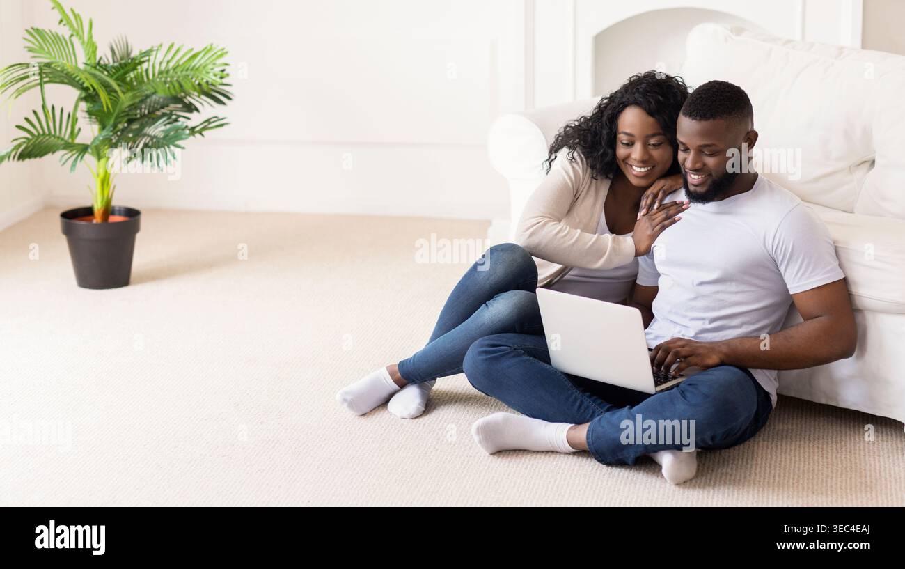 Giovane coppia che lavora insieme su un notebook mentre si siede comodamente sul pavimento Foto Stock