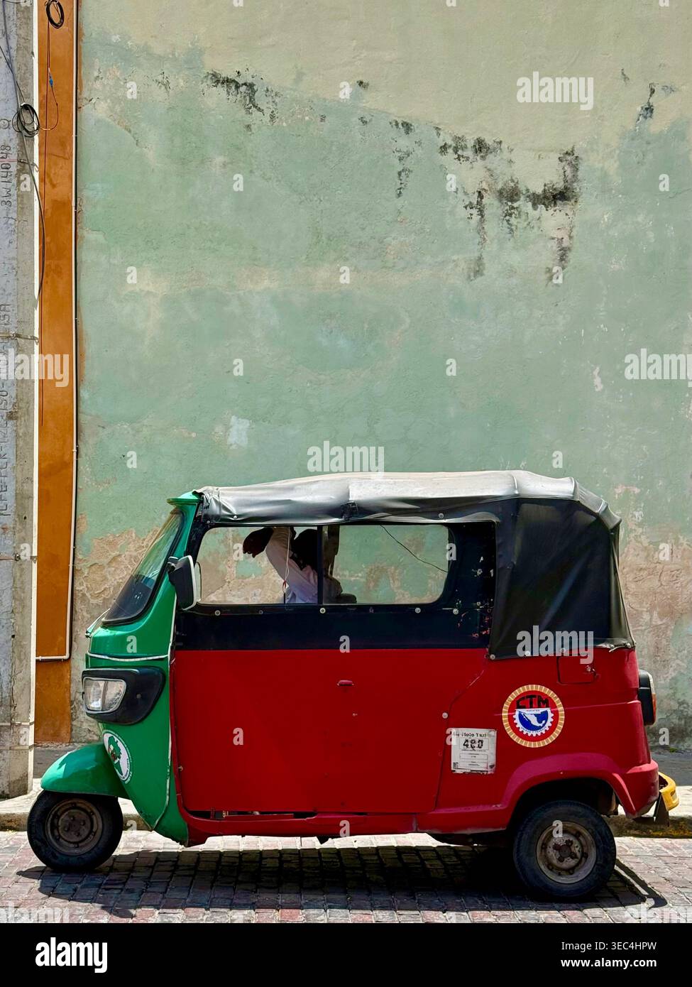 Colorato mototaxi a tre ruote parcheggiato contro un muro pastello intempestivo a Mérida, Yucatán, Messico Foto Stock