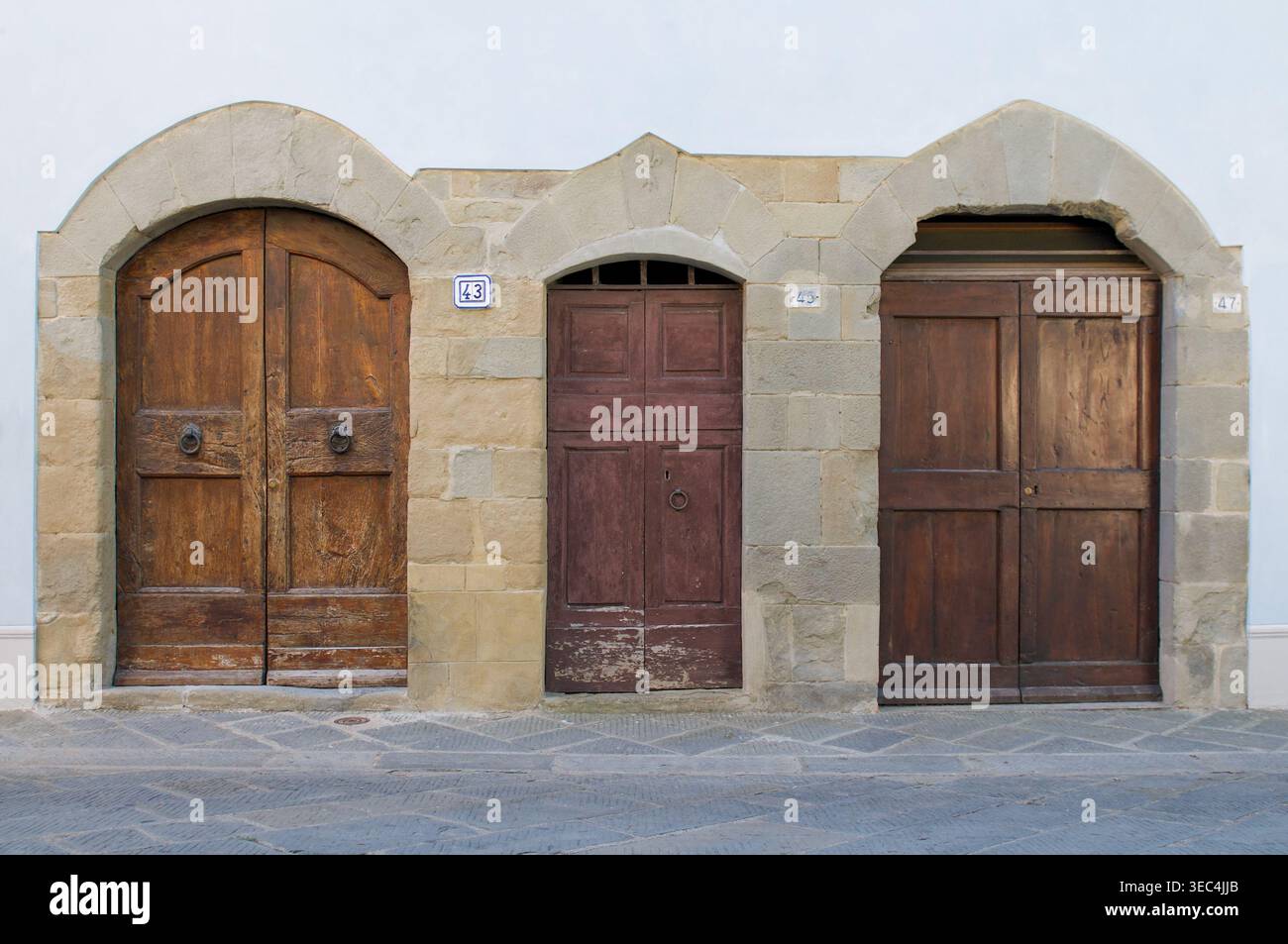 Vista frontale di 3 porte in legno di diverse forme e tipi di legno su un edificio residenziale esterno in Toscana, Italia Foto Stock