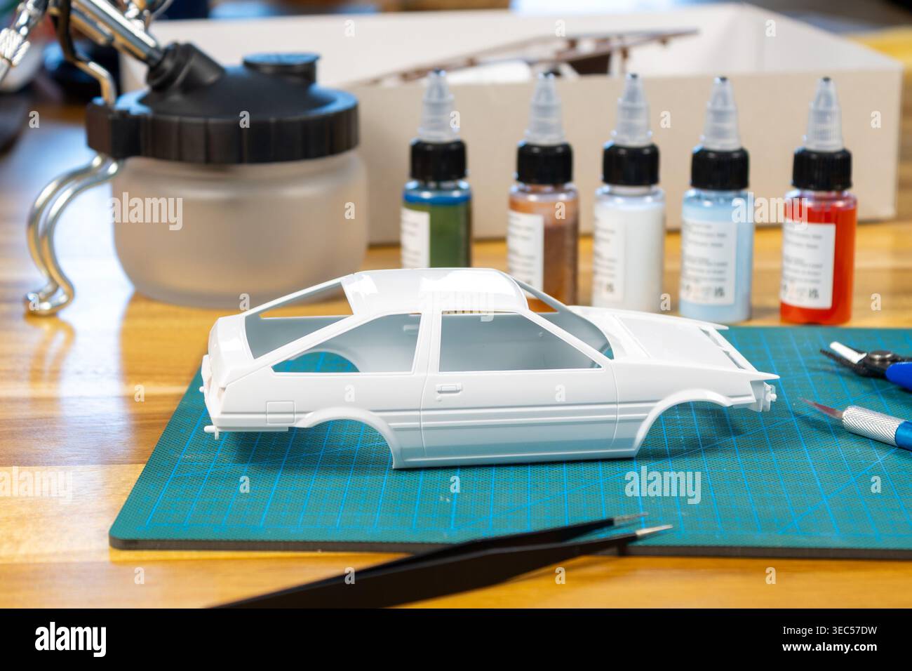 Primo piano del kit per auto modello non verniciato con strumenti e vernice sul tappetino da taglio – area di lavoro modellazione della bilancia Foto Stock