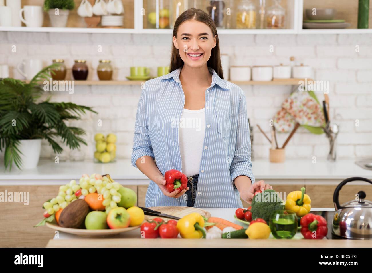 Donna che prepara verdure fresche in una cucina luminosa piena di prodotti colorati Foto Stock