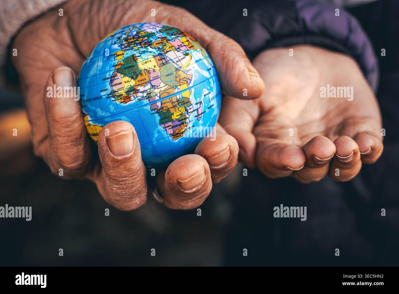 Mani anziane che donano un piccolo globo a mani più giovani, simbolo del futuro, della sostenibilità e della responsabilità Foto Stock